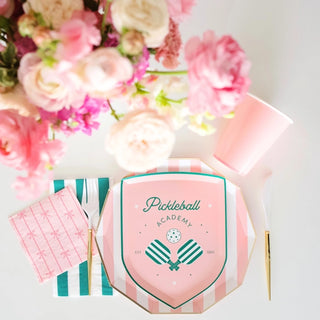 A bird's-eye view of a pastel-themed flat lay with eco-conscious Bonjour Fête Le Pickleball Small Plates stationery, a pen, stylish notebooks, and a bouquet of pink flowers, creating an aesthetic and organized workspace