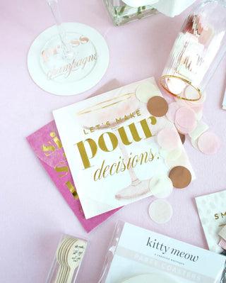 A flat lay of party-themed stationery, including Kitty Meow Boutique's "Let's Make Pour Decisions - Cocktail Party Napkins," confetti, and a "Kitty Meow" coaster set on a light pink background, perfect for bridal showers.