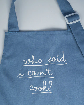 A blue Pop! Party Supplies Linen Cooking Apron with white text that reads "who said i can't cook?" in a casual handwritten font.