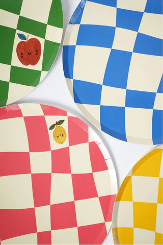 Four Little Chef Checkered Paper Dinner Plates by Pop! Party Supplies in green, blue, pink, and yellow make for perfect simple birthday party decor. The sustainable FSC paper plates feature charming illustrations: an apple on the green plate and a lemon on the pink one.