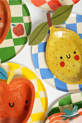 A variety of colorful die-cut party plates featuring smiling fruit designs, including an apple and a lemon, displayed on a white background. These Pop! Party Supplies Little Chef Dessert Party Plates are made from sustainable FSC paper.