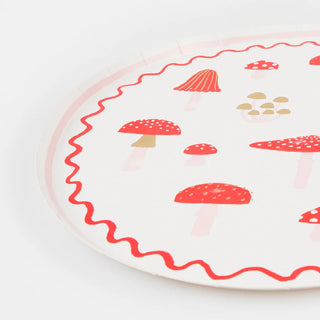 The Merry Mushrooms Dinner Plates by Meri Meri feature a round white design adorned with red and tan mushroom illustrations, a red wavy border along the edge, and festive gold foil details.