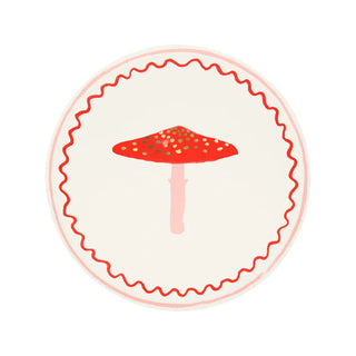 The Merry Mushrooms Side Plates by Meri Meri feature a central illustration of a red and white mushroom, encircled by a wavy red border on a white background, all embellished with gold foil details to create a festive design.