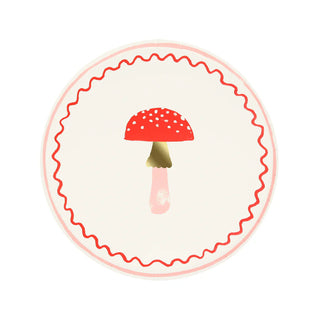 A stylized illustration of a red mushroom with white spots sits in the center of a cream-colored circle, bordered by a wavy red line and accented with gold foil details. The Merry Mushrooms Side Plates by Meri Meri are perfect for adding a touch of whimsy to any festive plate design or small paper plates set.