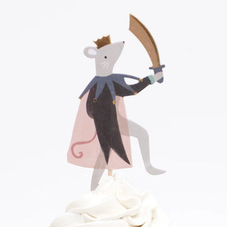 Illustration of a mouse donning a cape and crown, victoriously wielding a sword atop a white frosted cupcake, presented in an elegant gold foil cupcake case from the Nutcracker Cupcake Kit by Meri Meri.