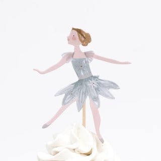 An illustration of a ballerina cake topper from the Nutcracker Cupcake Kit by Meri Meri, elegantly posed in a silver tutu on a swirl of white frosting, nestled among gold foil cupcake cases. Perfect for adding charm and grace to your Christmas cupcake display.