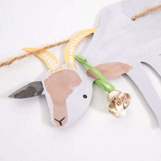 A paper cutout of a goat with a bell hanging from its neck on a green string is part of the "On The Farm Large Garland" by Meri Meri, perfect for adding a rustic touch to your birthday party decoration.