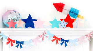 A shelf decorated with paper stars, a paper rocket, a small disco ball, and a Patriotic Paper Bow Garland - 4th of July by Kailo Chic alongside a banner with red, white, and blue pennant flags makes perfect party decorations for the 4th of July.