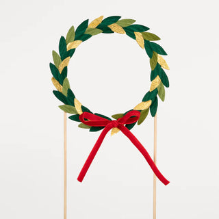 A festive Paper Wreath Cake Topper on a wooden stick adorned with a velvet bow by Meri Meri.