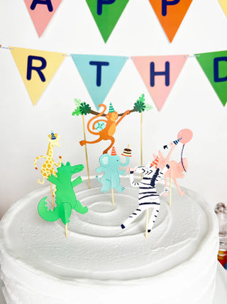 Using Merrilulu's Party Animals - Cupcake Toppers & Wrappers, you can create a stunning white frosted cake adorned with adorable animal figurines in party hats, including a monkey, giraffe, alligator, elephant, zebra, and flamingo. Complete the look with a vibrant triangular "HAPPY BIRTHDAY" banner to achieve the perfect setup for an animal-themed party.