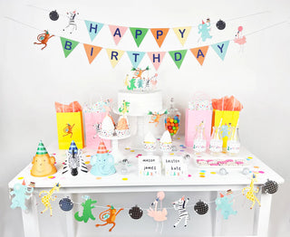 A birthday party table adorned with the Party Animals - Garland from Merrilulu, featuring gift bags, party hats, and a vibrant "Happy Birthday" banner. Perfectly crafted for an animal-themed birthday celebration, it showcases adorable animal decorations, candy jars, labeled drinks, and sparkly disco balls to add a touch of flair.