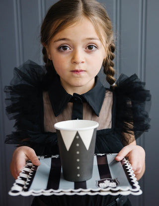 A little girl holding a black and white plate with a cup of coffee at a haunted house party using My Mind's Eye Party More Lapel Paper Party Cups.