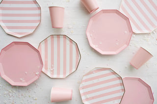 Elegant Petal Pink Signature Cabana Stripe Plates by Bonjour Fête, including cups, scattered on a white surface with confetti, suggesting a festive or celebratory occasion with a pastel theme.
