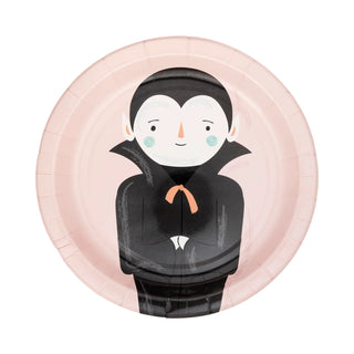 Introducing the Pink Monster Plate Set by My Mind’s Eye: round paper plates featuring an illustrated vampire character with a pale face, black cape, and a small orange bow tie set against a light pink background—perfect for Halloween parties. This set will add a spooky yet fun touch to your celebration.