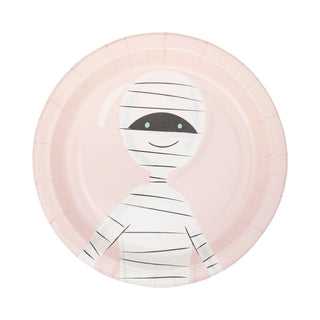 A paper plate from My Mind’s Eye Pink Monster Plate Set showcases a cartoon mummy design with a smiling face, black eyes, and white bandages on a light pink background—perfect for Halloween parties.