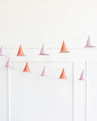 String lights featuring My Mind's Eye Pink Witch Hat Banner are hanging against a plain white wall, adding a touch of whimsical holiday decorations perfect for Halloween decor.