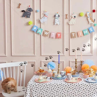 A whimsical pet party setup with a "pawty time" banner, playful animal decorations, a spotted tablecloth, pastel balloons, and a brown fluffy dog beside a table laden with Meri Meri Puppy Face with Droopy Ears Cups.