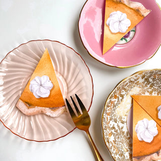 Three slices of Pumpkin Pie Party Punchies with whipped cream on top are served on decorative plates. A gold fork is placed on the leftmost plate, surrounded by festive decor that adds a charming touch to the scene.