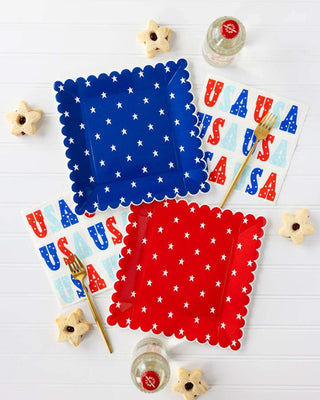 Patriotic table setup featuring star-spangled blue and red napkins, decorative usa letters, star-shaped cookies, a Red and Blue Star Paper Plate Set by My Mind's Eye, and refreshing beverages, ready to celebrate an American holiday.