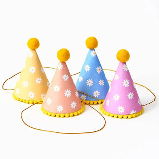 Four Paper Source Retro Daisy Party Hats, featuring vibrant colors and yellow pom-poms, arranged in a row, add a festive touch to any celebration.