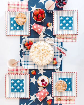 Table set with a star-themed design, featuring a large pie in the center surrounded by strawberries, individual pies on **Striped Scallop Plates by My Mind’s Eye**, cups, and bowls of berries. The red, white, and blue color scheme completes this summer coastal style for a patriotic celebration.