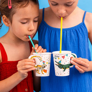 Two young children drink from Talking Tables Safari Animal Paper Cups with illustrations, using colored straws. One child wears a red dress, and the other wears a blue dress against a blue background.