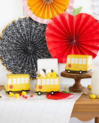 Decorative paper school bus boxes and a large Apple Shaped Napkin by My Mind’s Eye are displayed on a table, surrounded by colorful paper fans, perfect for back to school celebrations.