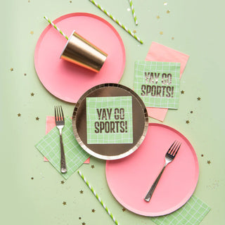 Table setup with Jollity & Co Shades Gild Dessert Plates, two forks, a gold cup, green napkins with "Yay Go Sports!" text, and star-shaped confetti on a pastel green background.