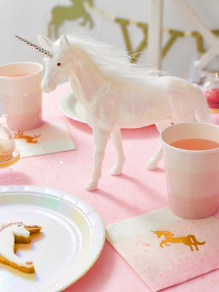 A pink table with unicorn-themed decorations, including a unicorn figurine, pink cups, unicorn-shaped cookies, and Small Unicorn Napkins by Talking Tables is perfect for any kids party.