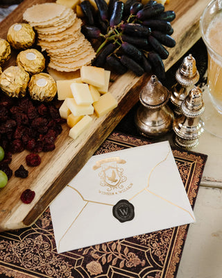 A tray featuring cheese, crackers, grapes, chocolates, and dried cranberries alongside a sealed envelope and ornate salt and pepper shakers is elegantly accented with My Mind’s Eye Spellbound Envelope Napkins.