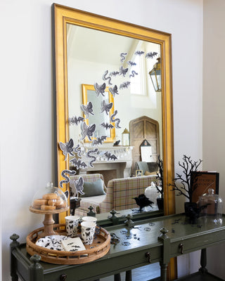 A large, gold-framed mirror on a green console table decorated with 3D bat and snake stickers sets the stage for a spooky celebration. On the table, a My Mind’s Eye Spooky Icons Plate holds treats alongside Halloween-themed cups and various eerie decorations.