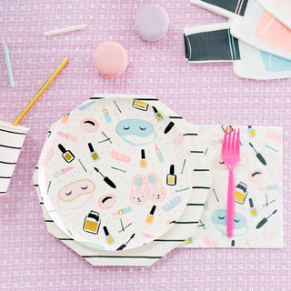 A pastel-themed slumber party table setting featuring a whimsically patterned paper plate, Sweet Dreams Large Napkins, and vibrant pink utensils from Daydream Society, complemented by pastel macarons