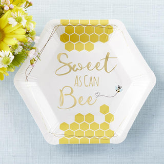 Hexagonal Kate Aspen Sweet as Can Bee Cocktail Plate with a yellow honeycomb design and the text "Sweet as Can Bee" printed in the center. A small bee graphic flies near the text, perfect for a baby shower. A bouquet of yellow and white flowers is beside the plate.