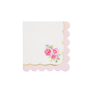 A neatly folded white Tea Party Rose Corner Paper Cocktail Napkin by My Mind’s Eye with scalloped pink edges, featuring a floral print of pink roses in one corner and delicate hints of gold foil.