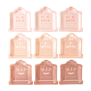 Image of nine peach-colored, tombstone-shaped decorations from My Mind’s Eye's Tombstone Plate Set. Perfect for a Halloween party, some inscriptions include "AL B. BACK," "B. WARE," and "RIP, Rest in Pieces." These spooky treats add a fun touch to your eerie festivities!