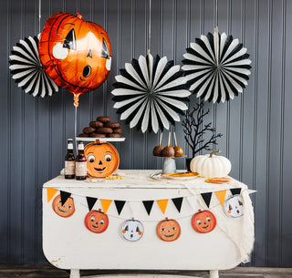 A table with Halloween decorations, including My Mind's Eye Vintage Halloween Trio Pumpkin Shaped Paper Plate Set and jack o' lantern balloons.