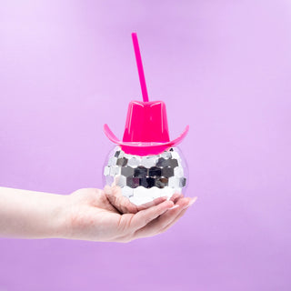 Hand holding the NPW Western Disco Cup, a silver disco ball-shaped cup with a pink cowboy hat lid and a pink straw, set against a purple background. Perfect for groovy hydration at your next bachelorette party!