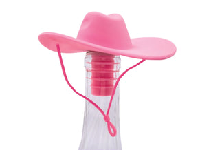 A Western Giddy Up Wine Stopper from NPW, featuring a premium silicone pink cowboy hat design, is placed on the neck of a clear glass bottle against a light purple background with white ray patterns, ensuring an air-tight seal.