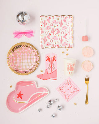Pink and gold foil themed party tableware, including My Mind's Eye's pink hat shaped paper plates, cups, and utensils, scattered with confetti and small disco balls on a white surface.