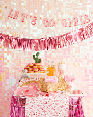 Party table with pink decor, snacks, and drinks for a cowgirl-themed event, featuring a "let's go girls" banner and cactus decoration with My Mind’s Eye Pattern Paper Table Runner.