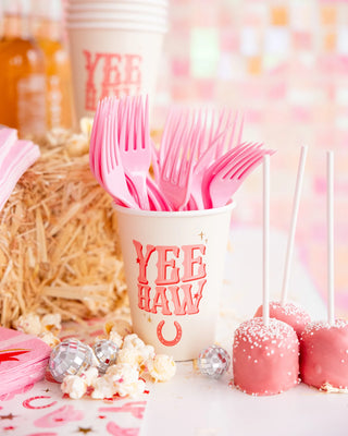 Yeehaw Paper Party Cups labeled "yeehaw" holding pink plastic forks, with cake pops, popcorn, and a straw bale in the background. - My Mind's Eye