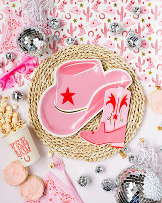 A vibrant party setup featuring a pink cowboy boot-shaped plate, popcorn, ice cream, Yeehaw Paper Party Cups by My Mind's Eye, and disco balls on a festive background.