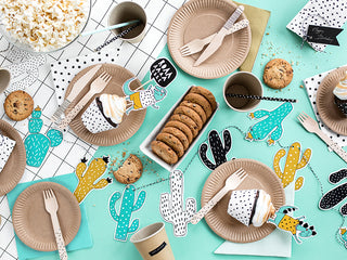 A table set with brown paper plates, wooden cutlery, cupcakes, cookies, popcorn, and cactus-themed decorations including a charming Cacti Garland by Party Deco on a mint green placemat—perfect for themed parties.