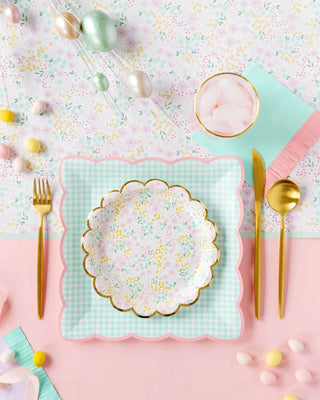 A table setting with Ditsy Floral Round Scallop Plates and My Mind's Eye forks on a pink and green background.