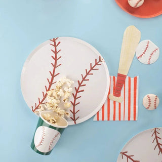 A baseball-themed party setup with plate designs mimicking a baseball, Meri Meri paper cups and serving utensils resembling a bat and glove, baseball-styled coasters, and popcorn adding a playful touch.