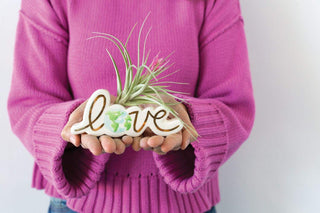 A woman holding a MINI EARTH LOVE BUDVASE by Accent Decor with the word love.