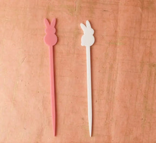 Two Easter Swizzle Sticks by Em and Me Studio on a pink background.