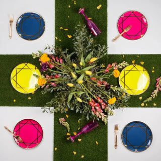 Overhead view of a vibrant outdoor dining setup with a floral centerpiece, Enchanté Dinner Plates - Mixed Pack by Jollity & Co, and utensils on a grass-themed tablecloth.