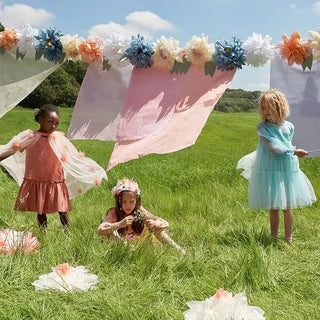 A group of children playing in a grassy field, surrounded by Meri Meri's Flowers In Bloom Giant Garland.