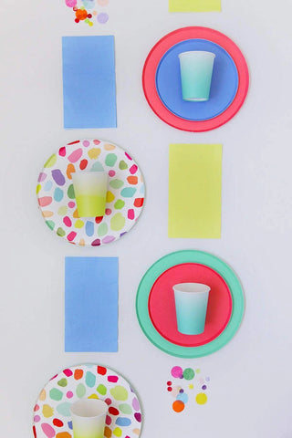 A cheerful and colorful arrangement of party supplies with Oh Happy Day Kindah Plates - 7 inch, plain cups, and matching napkins in coordinating colors of blue, green, and pink, artistically placed against a white background.